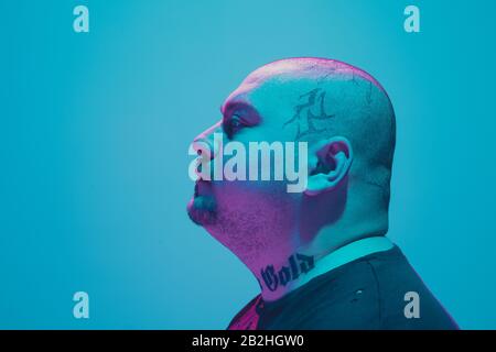 Portrait d'un gars hipster avec lumière néon colorée sur fond bleu studio. Modèle masculin d'humeur calme et sérieuse. L'expression faciale, le cyberpunk, le style de vie des millénaires et l'apparence. Mode. Banque D'Images