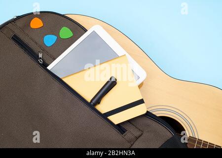 Sac souple pour guitare acoustique. Poche légèrement ouverte avec tablette, cahier en papier, stylo et sélection colorée sur fond bleu. Vue de dessus avec espace de copie Banque D'Images