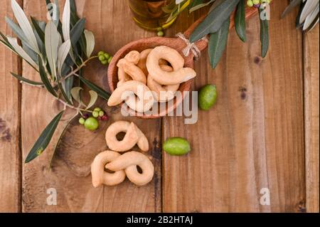 Le taralli est un snack-restaurant italien traditionnel typique de la cuisine régionale des Pouilles. Tarallini avec branches d'olive fraîches sur une table en bois. Espace de copie. Ci-Dessus. Banque D'Images