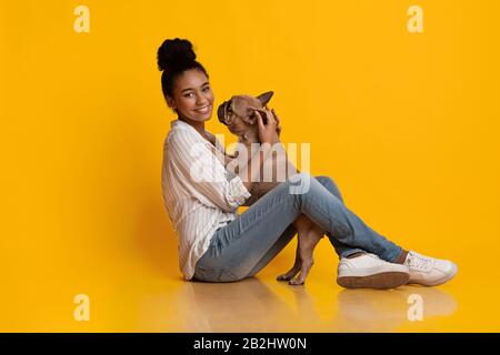 Happy Black Woman Embrassant Avec Son Bulldog Français Sur Fond Jaune Banque D'Images