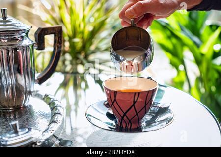 Couleurs vintage, lait versé dans la tasse, thé sur table en verre, main de la femme. Banque D'Images