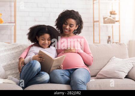 Petite afro fille lecture livre avec sa mère enceinte à la maison Banque D'Images