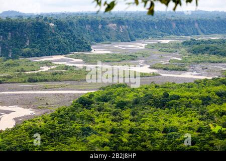 Une perspective surélevée montre une rivière boueuse sinueuse coupant à travers une large plaine inondable entourée d'une forêt verte dense et de falaises rocheuses abruptes. La rivière se divise en plusieurs canaux, créant Banque D'Images