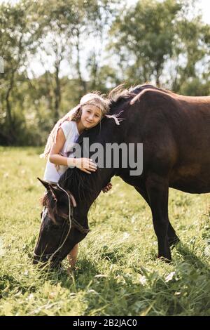 Petite jolie fille embrassant son cheval et beau coucher de soleil chaud dans le champ d'été à la campagne. Cheval et belle fille - meilleurs amis Banque D'Images