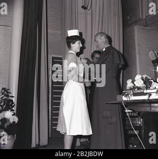 Années 1960, historique, une jeune femme, infirmière en uniforme recevant ses badges d'infirmière sur scène d'un prêtre en robe longue, Angleterre, Royaume-Uni. Banque D'Images