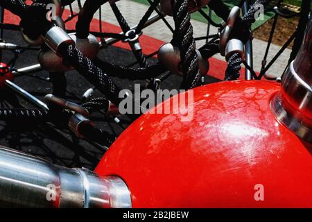 équipements d'escalade pour enfants dans un terrain de jeu et un parc public avec cordes en vinyle noires, pinces en acier inoxydable et grosses rotules en plastique rouge brillant. Banque D'Images