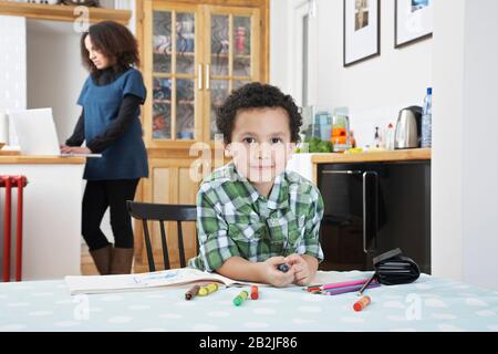 Portrait d'un garçon (5-6) assis à la table mère à l'aide d'un ordinateur portable en arrière-plan Banque D'Images