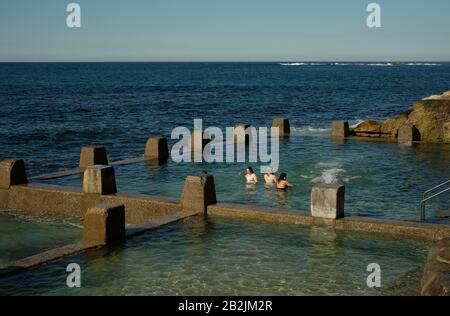 Trois jeunes femmes dans l'eau de mer froide de couleur bleu-vert des murs de la piscine crénelée, Ross Jones Rockpool, en bordure de l'océan Pacifique Sud, Sydney Banque D'Images