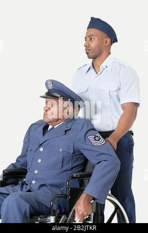 Cadet masculin aidant l'officier supérieur de l'armée de l'air en fauteuil roulant sur fond gris clair Banque D'Images