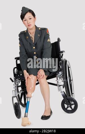 Portrait d'un militaire américain féminin dans un pied de prothèse en fauteuil roulant sur fond gris Banque D'Images