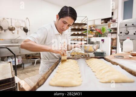 Un jeune boulanger masculin fait de la pâte dans une cuisine commerciale Banque D'Images
