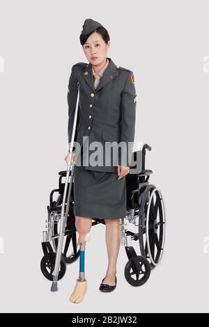 Officier militaire américain handicapé avec une béquille devant un fauteuil roulant sur fond gris Banque D'Images