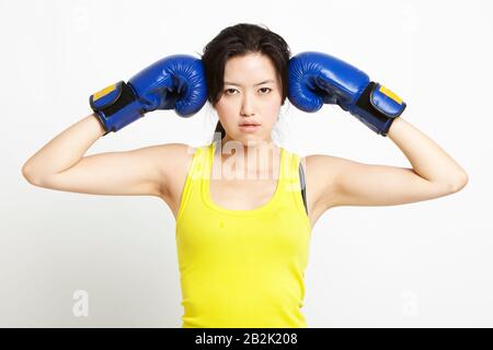 Portrait de la jeune femme asiatique dans un débardeur jaune portant des gants de boxe sur fond blanc Banque D'Images