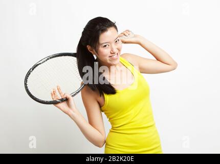 Portrait de la jeune femme asiatique tenant une raquette de tennis sur son épaule contre fond blanc Banque D'Images