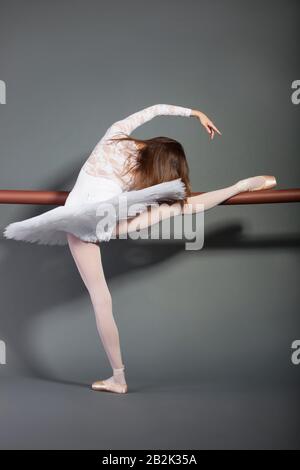 Danseuse de ballet jeune femme s'étirant au bar de ballet sur fond gris Banque D'Images