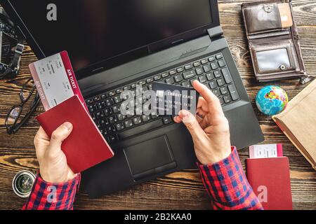 Préparez-vous à un voyage passionnant. Man livre des vols en tapant sur un ordinateur portable et en payant avec une carte de crédit sur un fond en bois. La vue du haut Banque D'Images