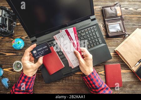 Préparez-vous à un voyage passionnant. Man livre des vols en tapant sur un ordinateur portable et en payant avec une carte de crédit sur un fond en bois. La vue du haut Banque D'Images