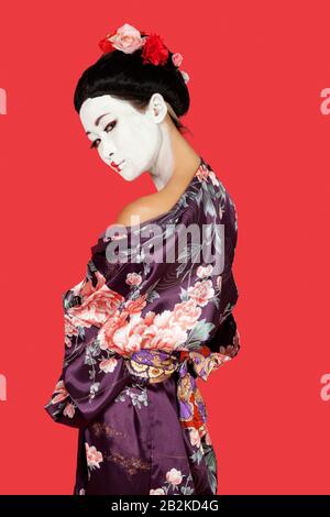 Portrait d'une femme japonaise dans un kimono debout sur fond rouge Banque D'Images