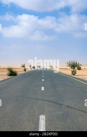 Photo verticale d'une route vide dans le désert avec ciel bleu et peu de nuages Banque D'Images