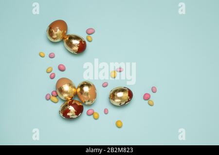 Oeufs de pâques brun-doré et bonbons de couleur dans des haricots de gelée sur fond bleu avec copyspace. Vue sur le dessus, plat Banque D'Images