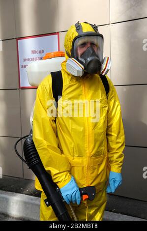 Paramédic portant un costume de protection jaune et masquez le coronavirus désinfectant à l'aide de l'atomiseur à dos motorisé. 26 Février 2020. Kiev, Ukraine Banque D'Images