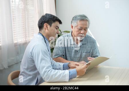 Vue de profil du médecin-conseil du cardiologue caucasien avec son patient asiatique aîné senior, à l'aide du fichier de document pendant la vérification et la prise Banque D'Images