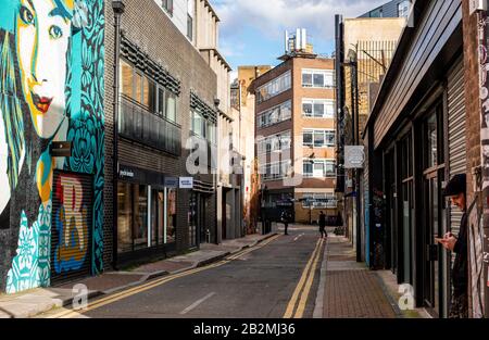 Un homme prend une pause dans une rue solitaire face à quelques œuvres d'art graffitis avec d'autres personnages dans la distance. Banque D'Images