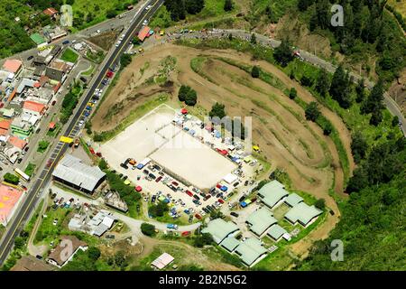 Une photographie aérienne montre une grande piste de terre avec plusieurs voies courbes, probablement pour des événements hors route ou de motocross, adjacente à une route pavée avec des véhicules. Une grande zone pavée rectangulaire, peut-être un Banque D'Images