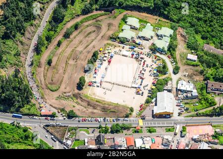 Une photographie aérienne montre une grande piste de terre avec plusieurs voies courbes, probablement pour une utilisation hors route ou de sport automobile, adjacente à un parking pavé rempli de véhicules et de petites structures avec du vert Banque D'Images