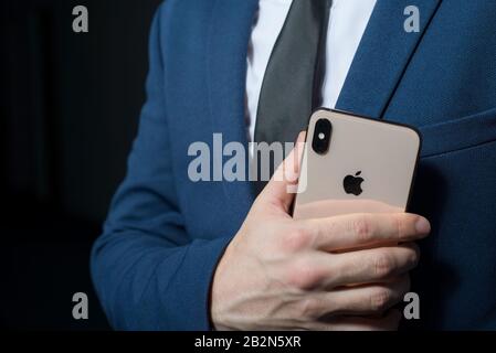 Zaporozhye. Ukraine. Février 2020. Gros plan portrait d'un jeune homme barbu dans un costume d'affaires tenant un iPhone XS dans sa main. Nouveau smartphone de Banque D'Images