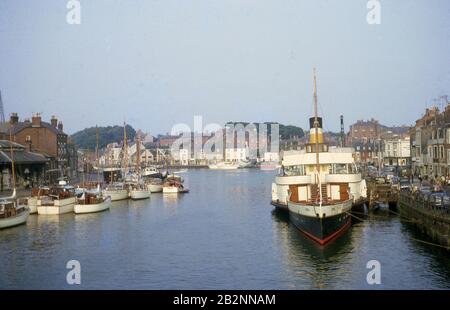 Années 60, historique, le vieux port de Weymouth, Dorset, Angleterre, un port protégé, avec de petits bateaux à voile en bois de l'époque et un bateau à pédales amarré. Banque D'Images