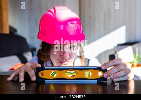 jeune architecte caucasien portant un chapeau de dur rose et des lunettes de protection, elle mesure la surface horizontale avec un outil bulle à bulle Banque D'Images