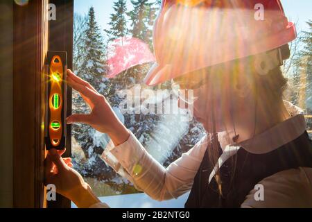 Femme inspecteur canadien de la construction utilisant un instrument de niveau esprit sur la fenêtre avec vue sur la neige en plein air en arrière-plan. Inspection avant achat à domicile Banque D'Images