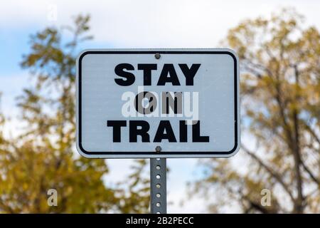 Restez sur le panneau métallique noir et blanc de Trail lors d'une journée ensoleillée d'automne. Banque D'Images