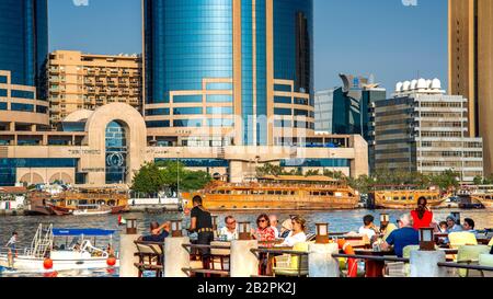 Dîner au café en bord de mer sur Dubai Creek, avec des bâtiments modernes en arrière-plan. En avant-plan avec des gens qui se socialisent. Banque D'Images