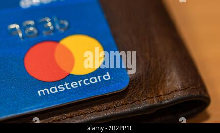 Logo Mastercard sur la carte bleue au-dessus du portefeuille marron placé sur une table. Banque D'Images