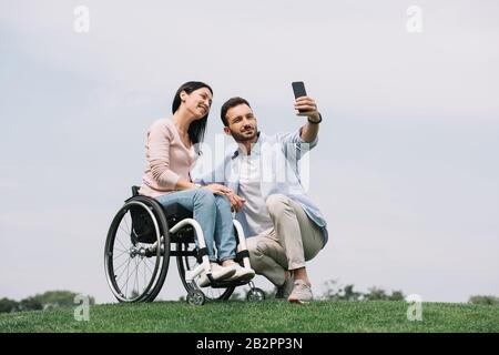 un jeune homme heureux prenant selfie sur son smartphone avec une petite amie souriante pour handicapés dans le parc Banque D'Images