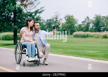 heureux homme embrassant la petite amie des handicapés et prendre selfie sur le smartphone dans le parc Banque D'Images