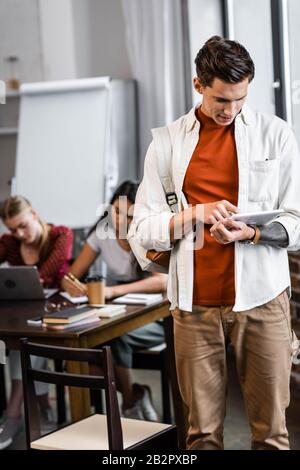 beau étudiant en chemise en utilisant une tablette numérique dans l'appartement Banque D'Images