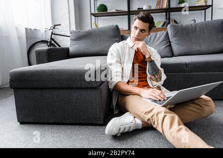 bel homme en chemise assis au sol et utilisant un ordinateur portable dans l'appartement Banque D'Images