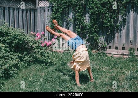 Drôle enfant adolescent fille faisant la roue de cartWheel sur l'arrière-cour. Enchanté joyeux enfant jouant en plein air. Style de vie heureux enfant et esprit de liberté concept. Saison Banque D'Images