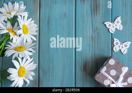 Daisies gros plan sur un fond bleu en bois avec des papillons et une boîte avec un cadeau. Contexte pour une bannière de félicitations. Anniversaire, réductions, Banque D'Images