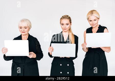 femmes d'affaires blondes tendance de trois générations en costume noir avec ordinateurs portables isolés en gris Banque D'Images