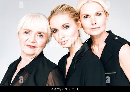 femmes blondes de trois générations en costume noir total isolé sur gris Banque D'Images