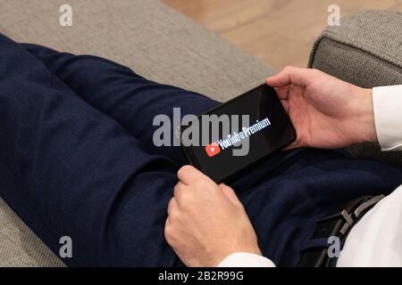 Homme assis sur un canapé tenant un iPhone comme le logo YouTube Premium est à l'écran. Banque D'Images