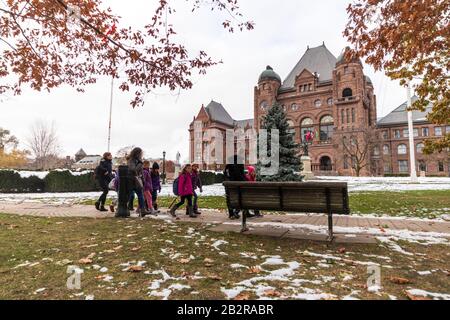 Un groupe de personnes se promenent sur un sentier devant l'Assemblée législative de l'Ontario, un après-midi enneigé. Banque D'Images
