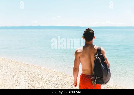 jeune homme voyageur avec sac à dos sur l'épaule seul au bord de la mer et regardant dans l'océan bleu cyan, profitant de voyage et de la nature Banque D'Images