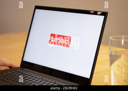 Personne assis sur un bureau à l'aide d'un ordinateur portable Lenovo avec le logo Lenovo à l'écran. Banque D'Images