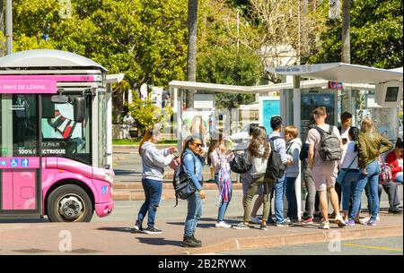 Cannes, FRANCE - AVRIL 2019 : foule de personnes en attente d'un bus à un arrêt de bus dans le centre de Cannes. Un petit bus électrique est stationné à proximité Banque D'Images