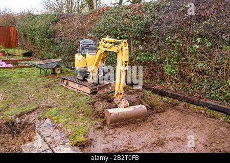 Cardiff, PAYS DE GALLES - JANVIER 2020: Mini pelle hydraulique creusant la pelouse dans le jardin arrière d'une propriété résidentielle Banque D'Images